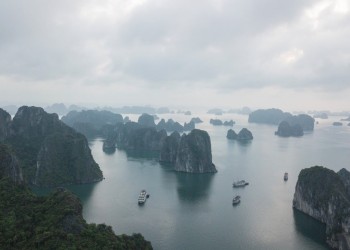 An array of small tropical islands with high cliffs and jungle on top. Boats sail between them.