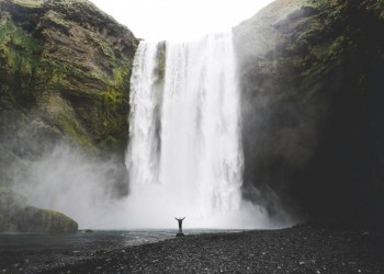 A huge waterfall in the background and a small figure standing at the bottom, raising their arms.